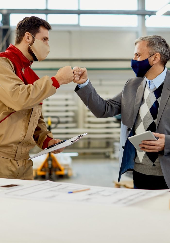 Happy businessman and manual worker greeting with fists while working at carpentry workshop.